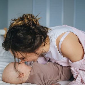 Woman in White and Pink Striped Long Sleeve Shirt Playing with Baby Lying on Bed