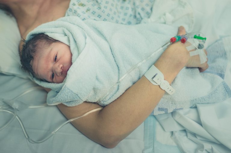 Swaddled newborn baby wearing a hospital identification bracelet resting after birth