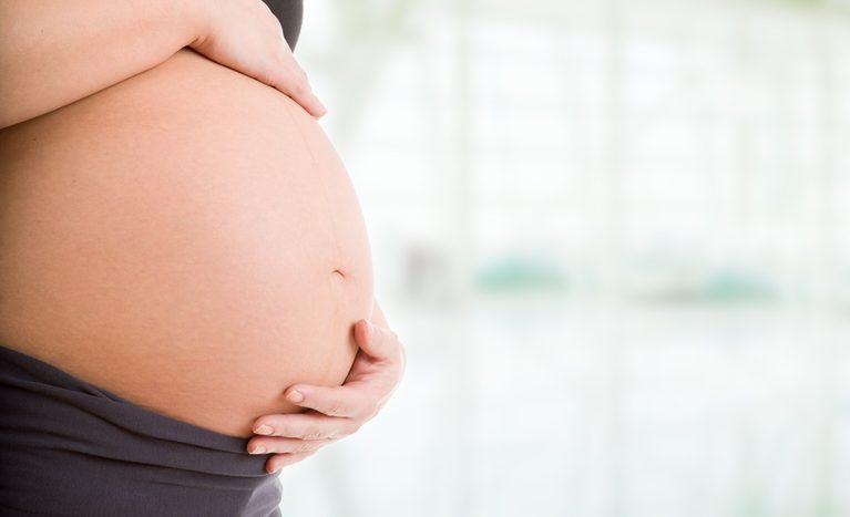 A close-up shot of a pregnant woman holding her hands over her baby bump.