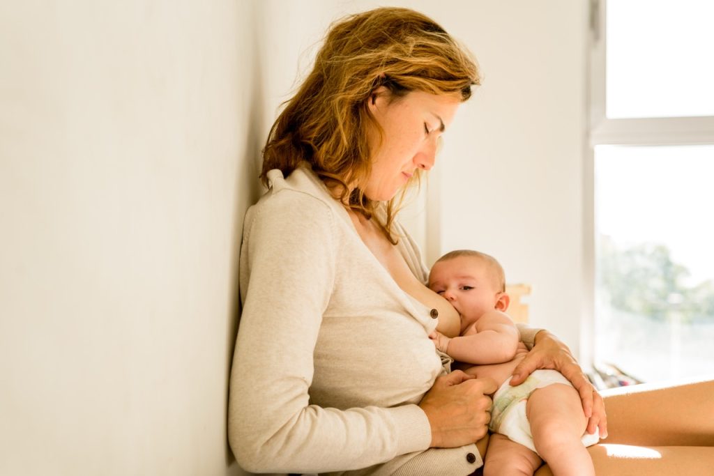 Mother sitting on a bed and lovingly holding her newborn baby close to her chest.
