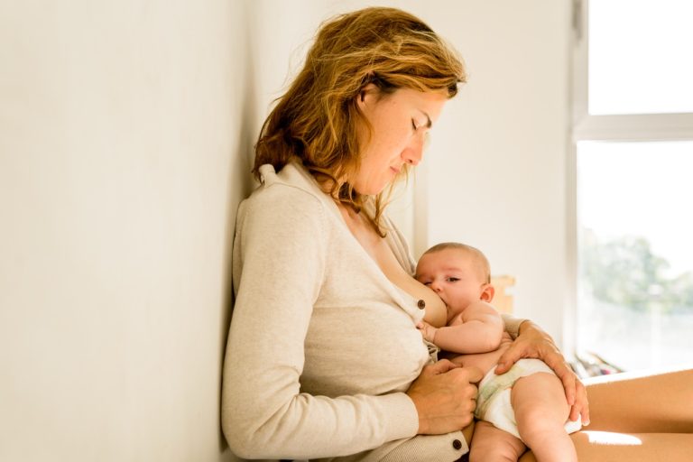 Mother sitting on a bed and lovingly holding her newborn baby close to her chest.