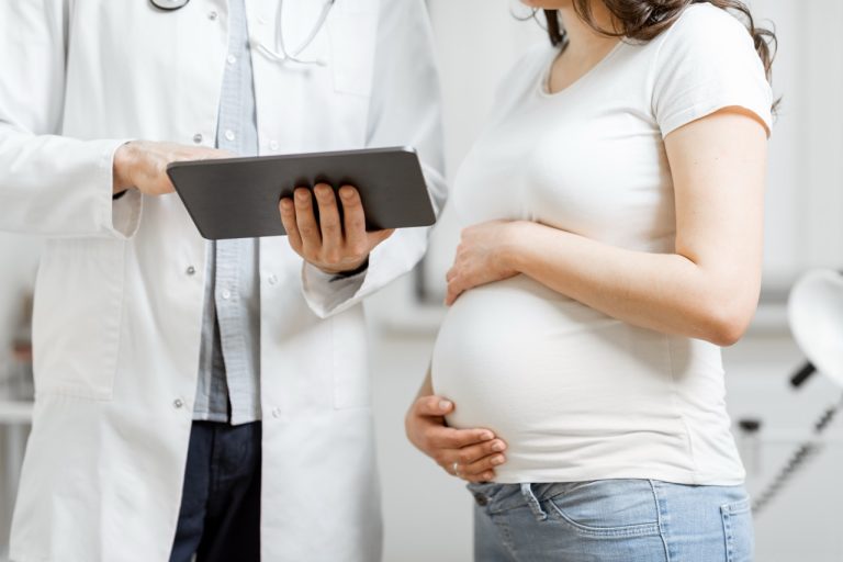 Healthcare provider measuring a pregnant woman's abdomen with a tape measure during a prenatal exam.