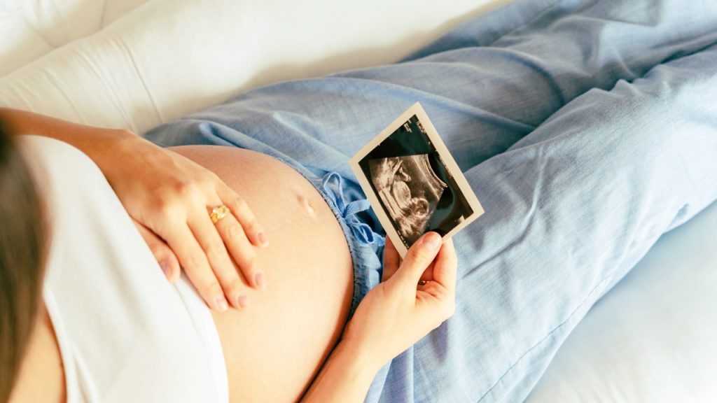 Close-up of a pregnant woman sitting comfortably with her hands resting gently on her belly.